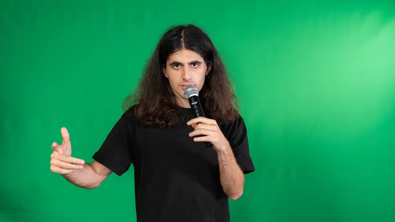 Ash Kazaryan holding a microphone against a green backdrop